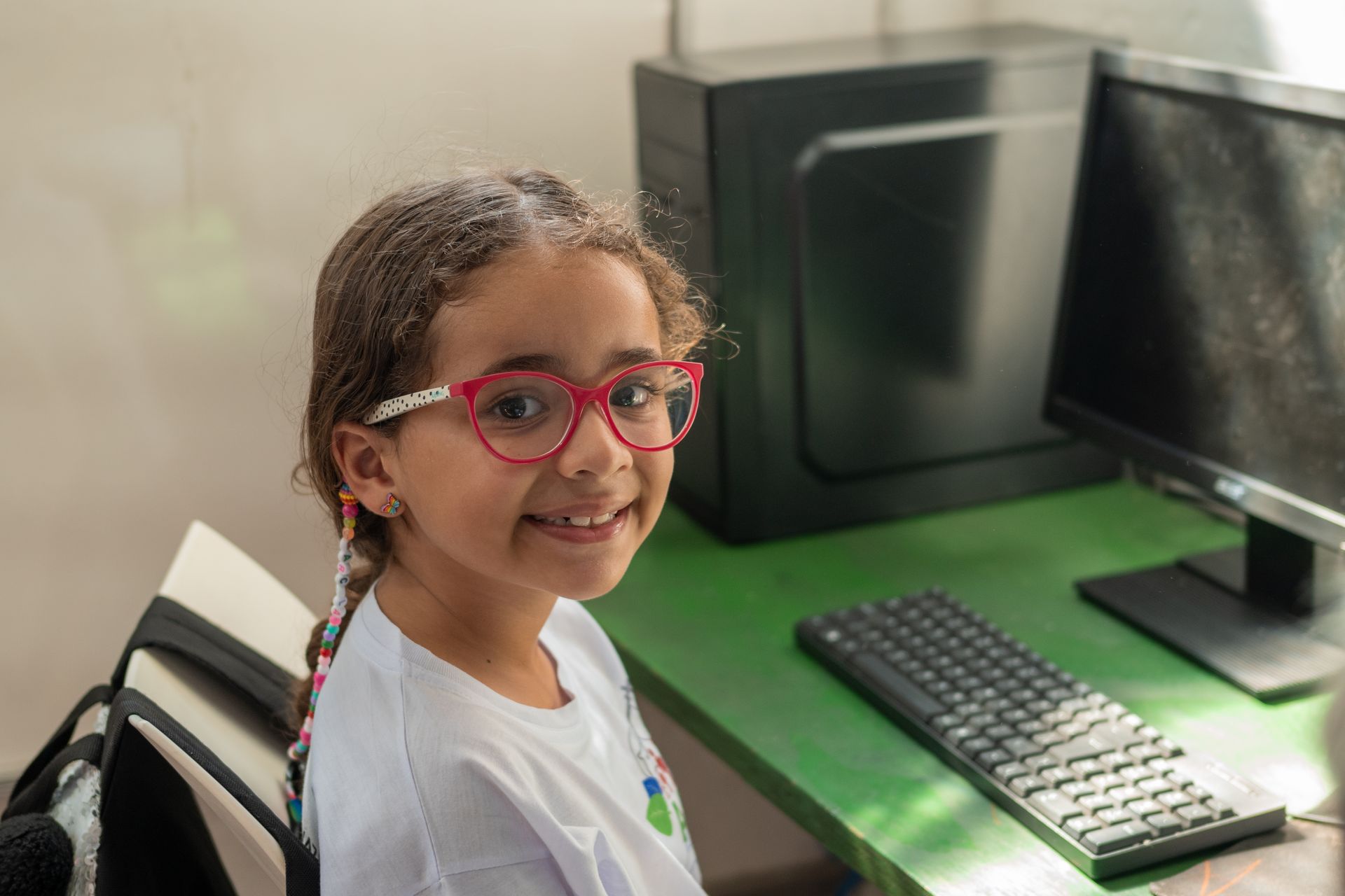 a little girl wearing glasses is sitting at a desk in front of a computer .