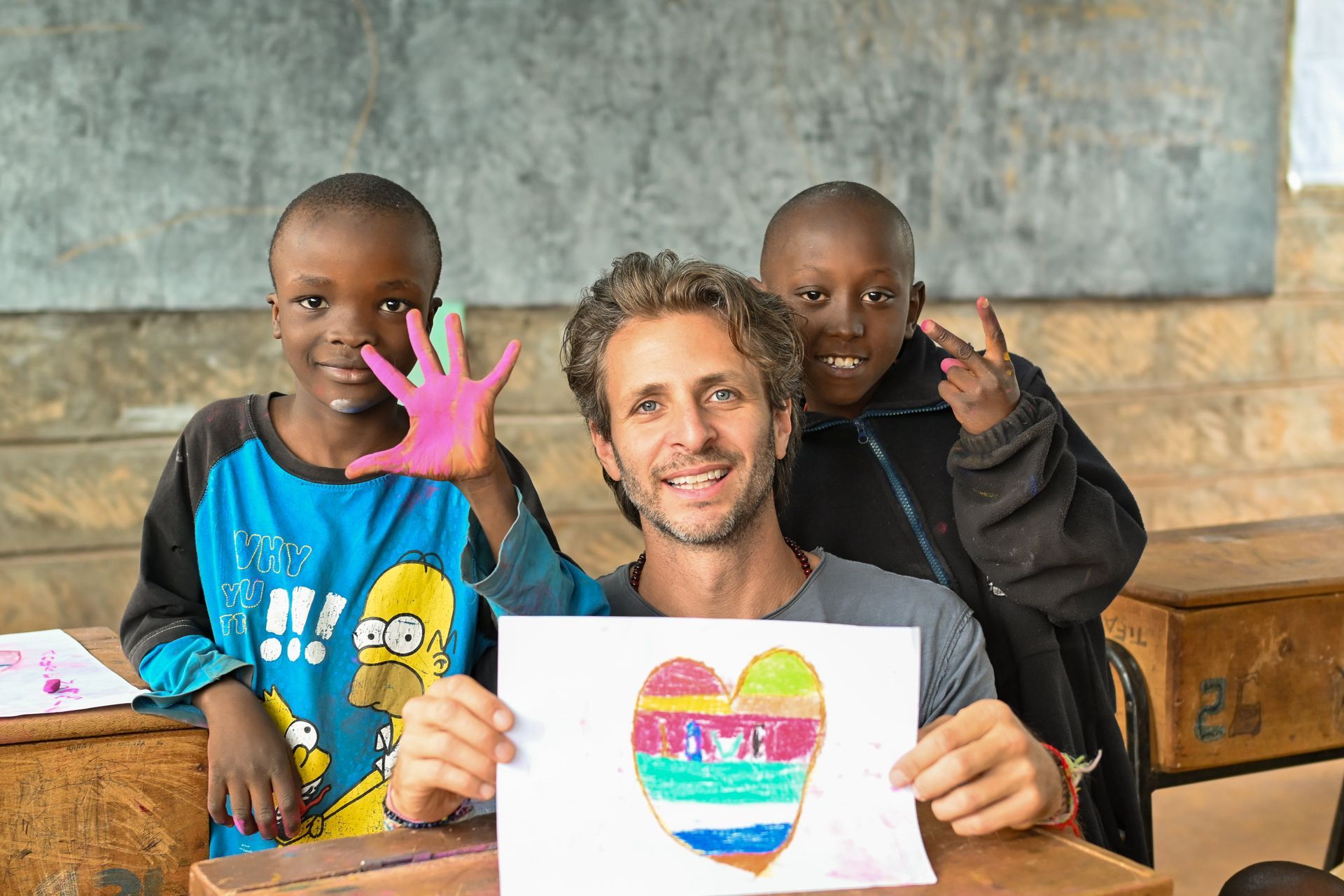 justin garcia artist is holding a drawing of a heart in front of two children. orphaned starfish foundation andy stein