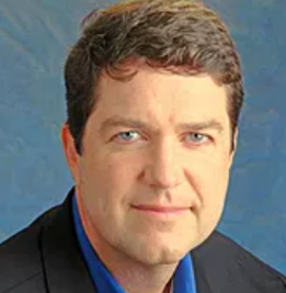 A man in a suit and blue shirt is smiling for the camera. greg ostean