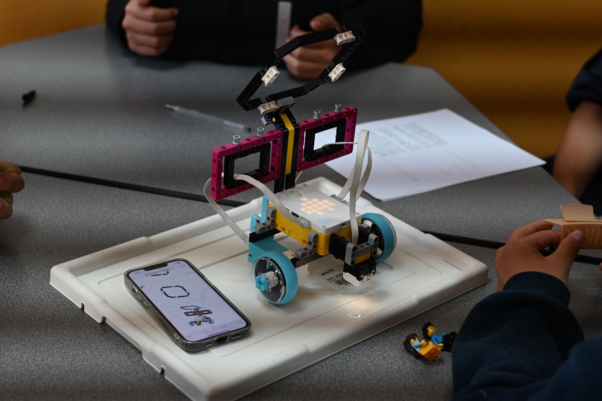 LEGO robot on a white tray with a smartphone, surrounded by Students.  orphaned starfish foundation  andy stein OSF Robotics Initiative stem education