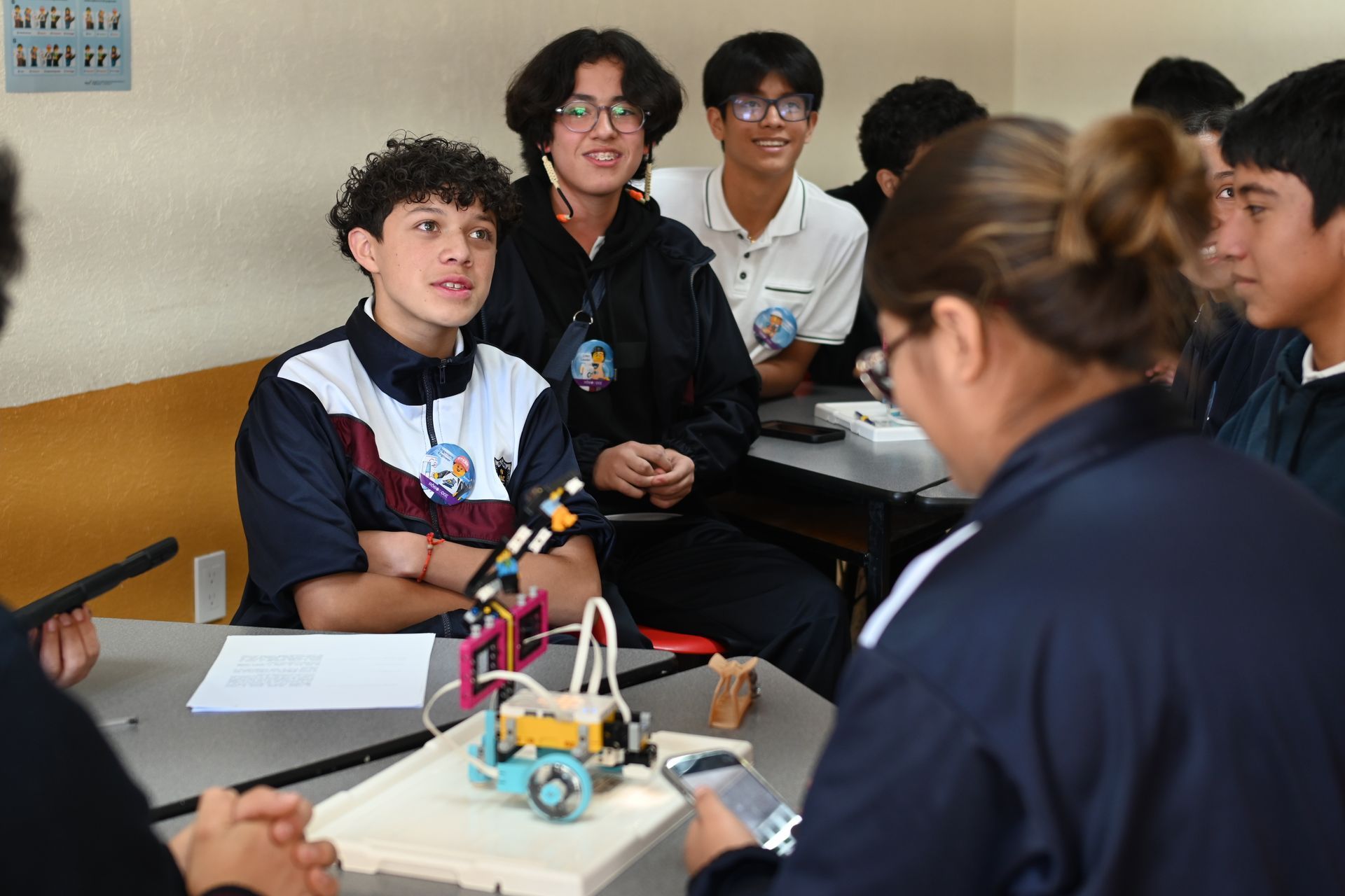 A group of students in a classroom are gathered around a small robot.  Students observing a demo of a small robotic device. orphaned starfish foundation  andy stein OSF Robotics Initiative stem education
