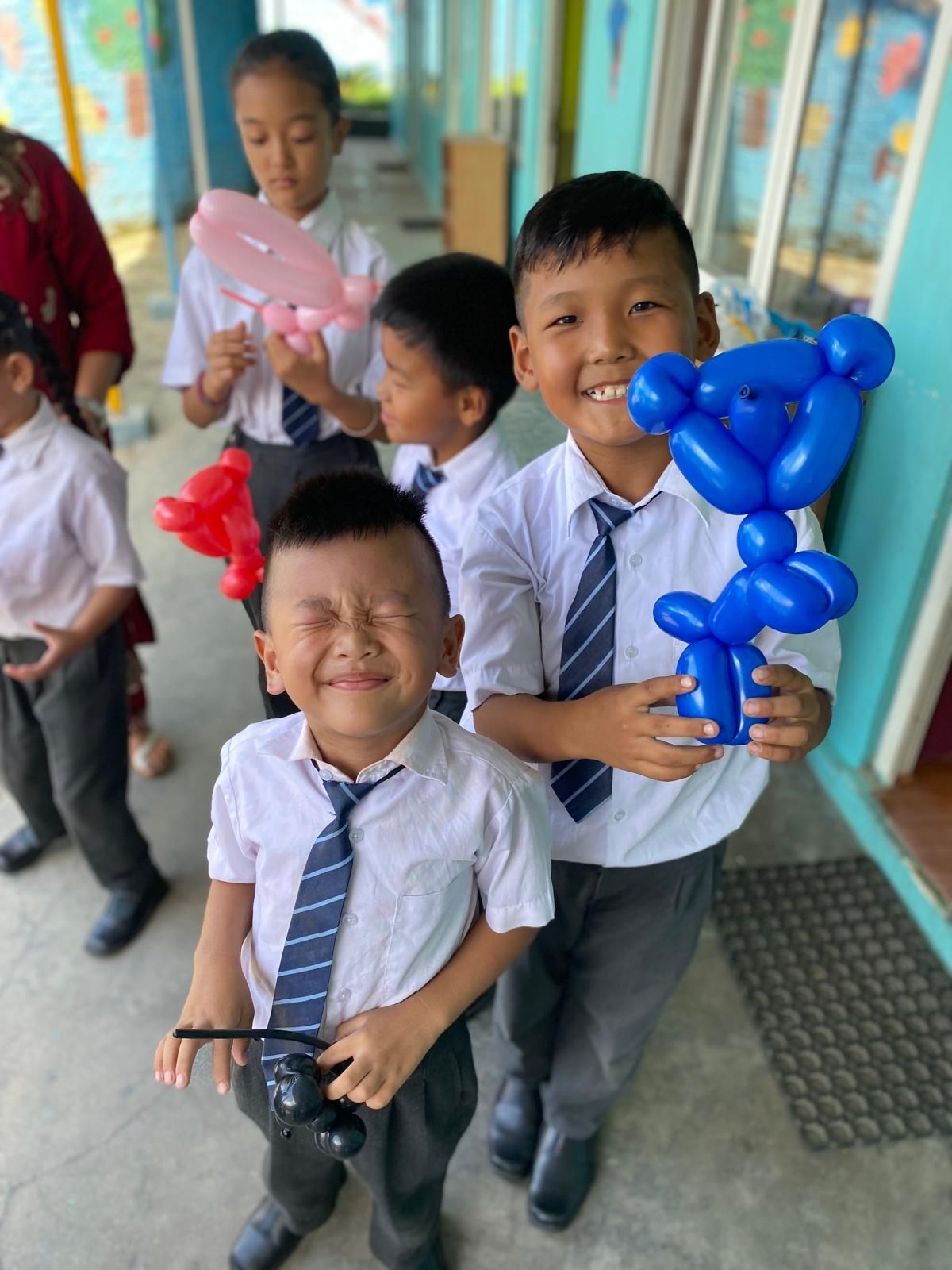 A group of Nepalese children in school uniforms and ties are holding balloons.  Andy Stein of orphaned starfish 