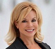 A woman with blonde hair and a black jacket is smiling for the camera.