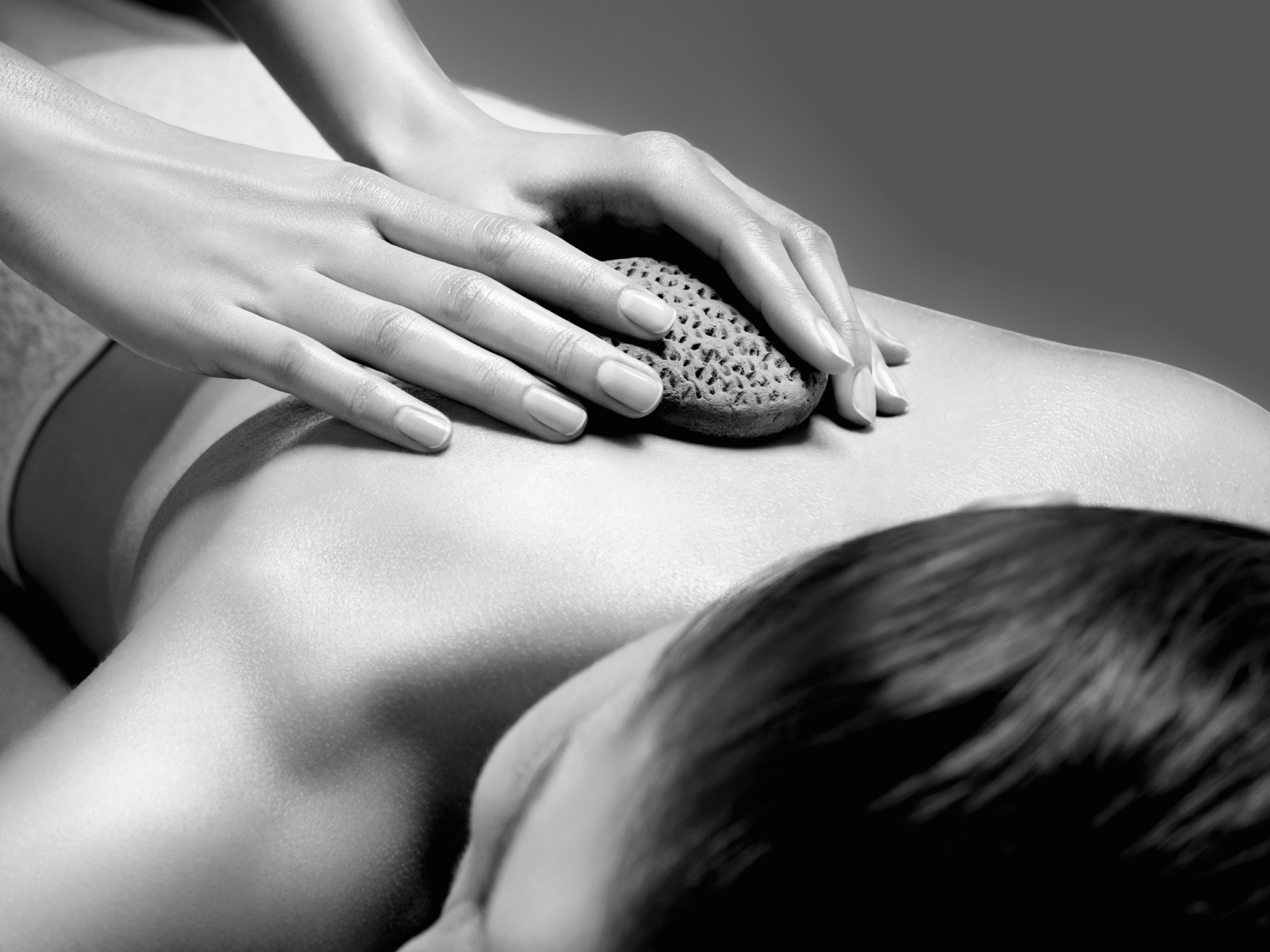 A woman is getting a massage with a rock on her back.