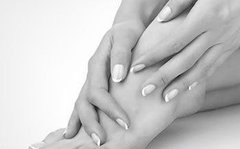 A black and white photo of a woman 's hands and feet with white nails.