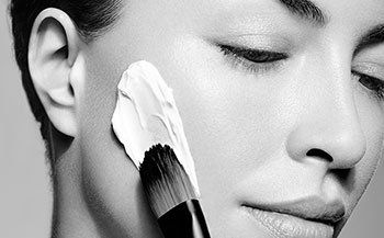 A woman is applying makeup to her face with a brush.