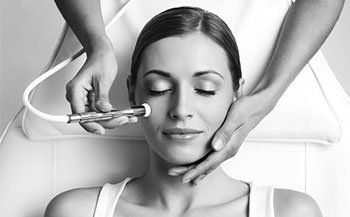 Black and white image of womans face and a hand with a brush applying a lotion in a beauty spa