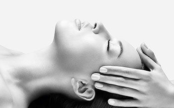 A woman is laying down with her eyes closed and her hands on her face.