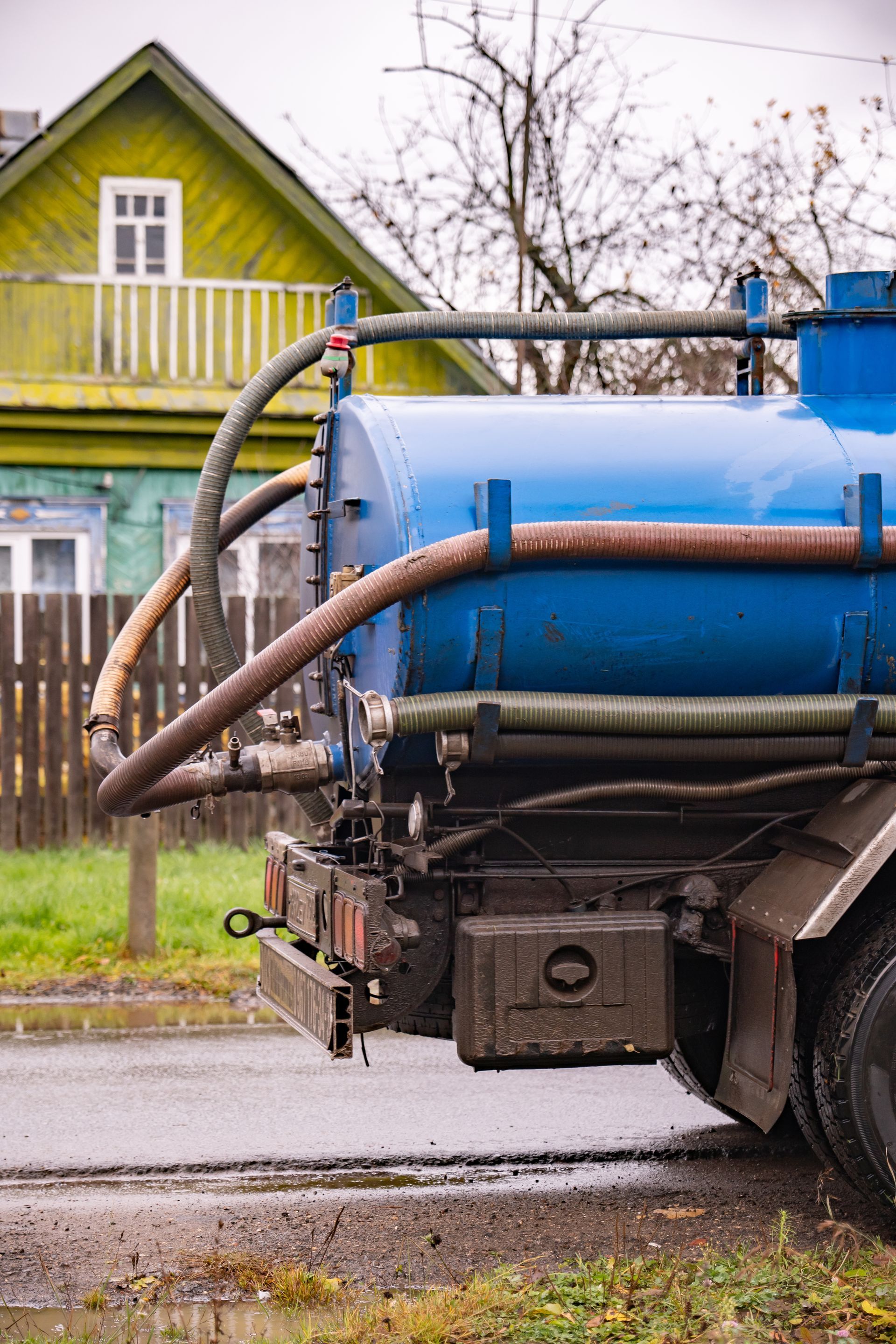 Commercial septic pumping vehicle parked near home with vacuum tank and extended hoses.