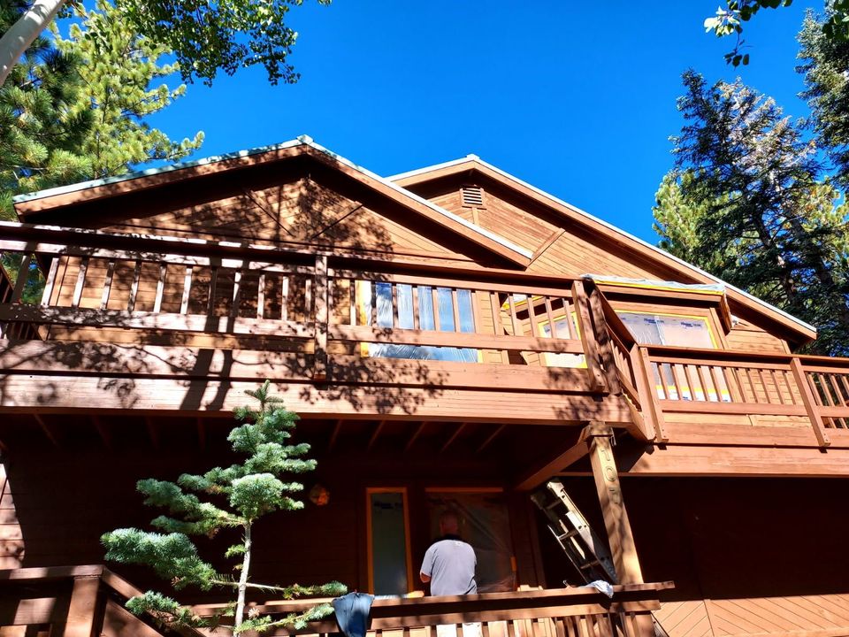 Wooden cabin with balcony, person on porch, blue sky, and trees.
