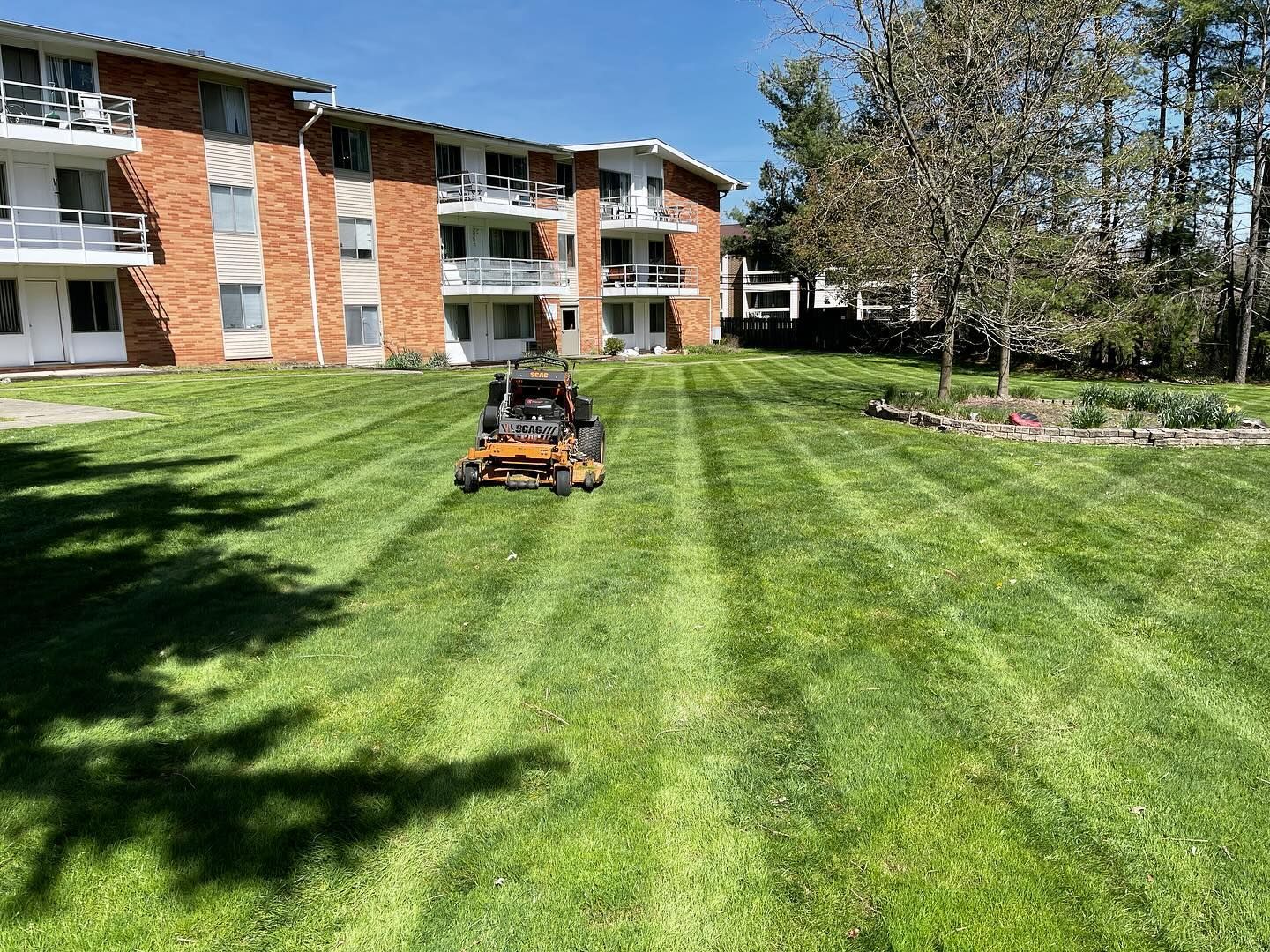 A lawn mower is cutting a lush green lawn in front of a building.
