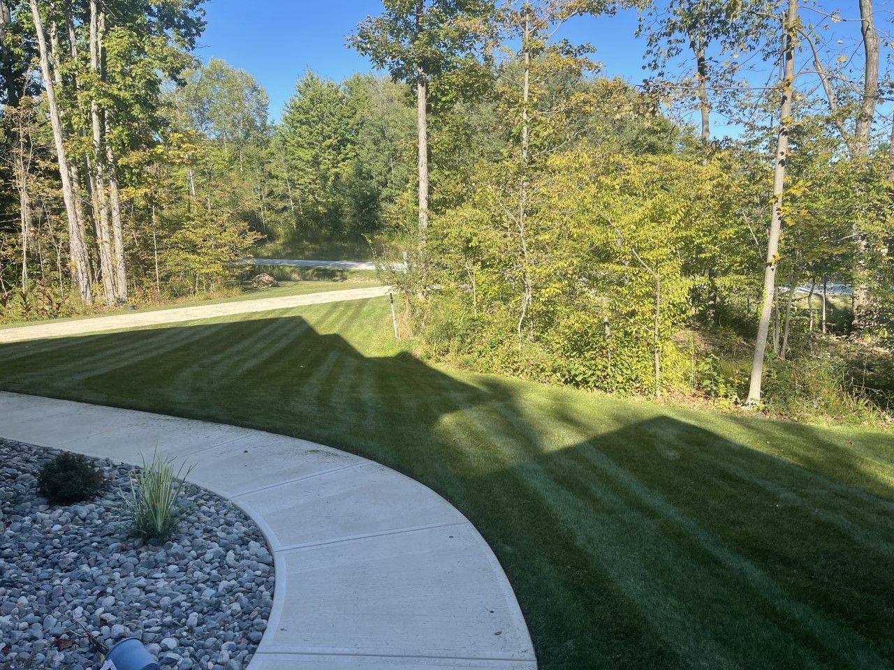 A walkway leading to a lush green lawn with trees in the background.