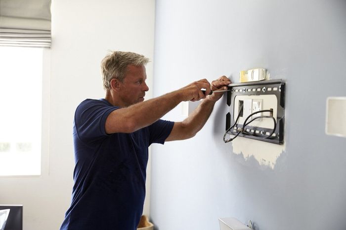 Man Fitting Bracket For Flat Screen TV  — Domestic Electrical in Tamworth, NSW