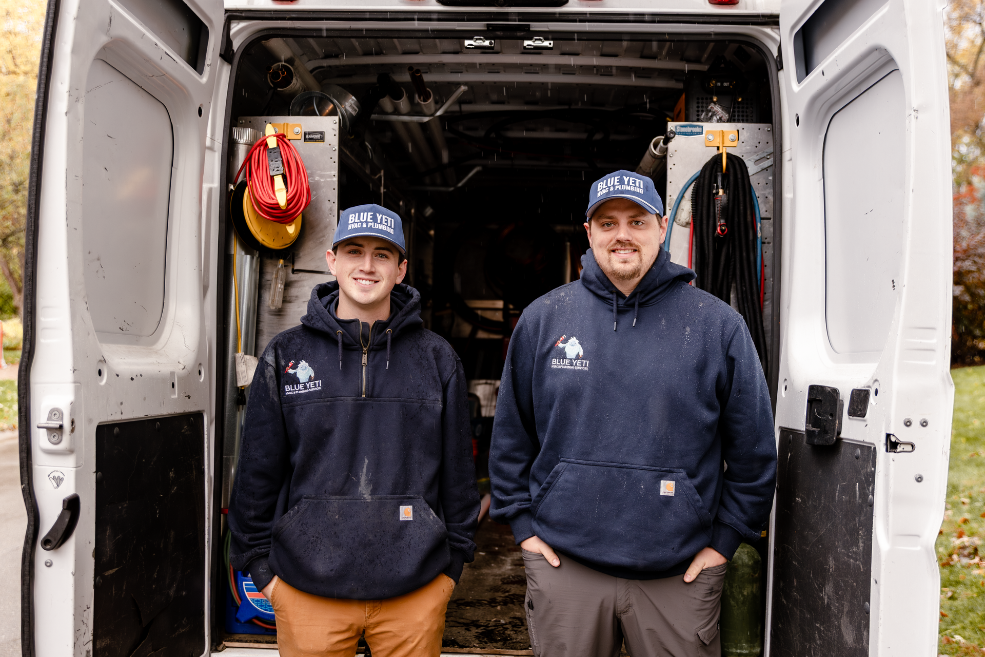 Two men in navy hoodies stand inside a van. Tools and equipment are visible.