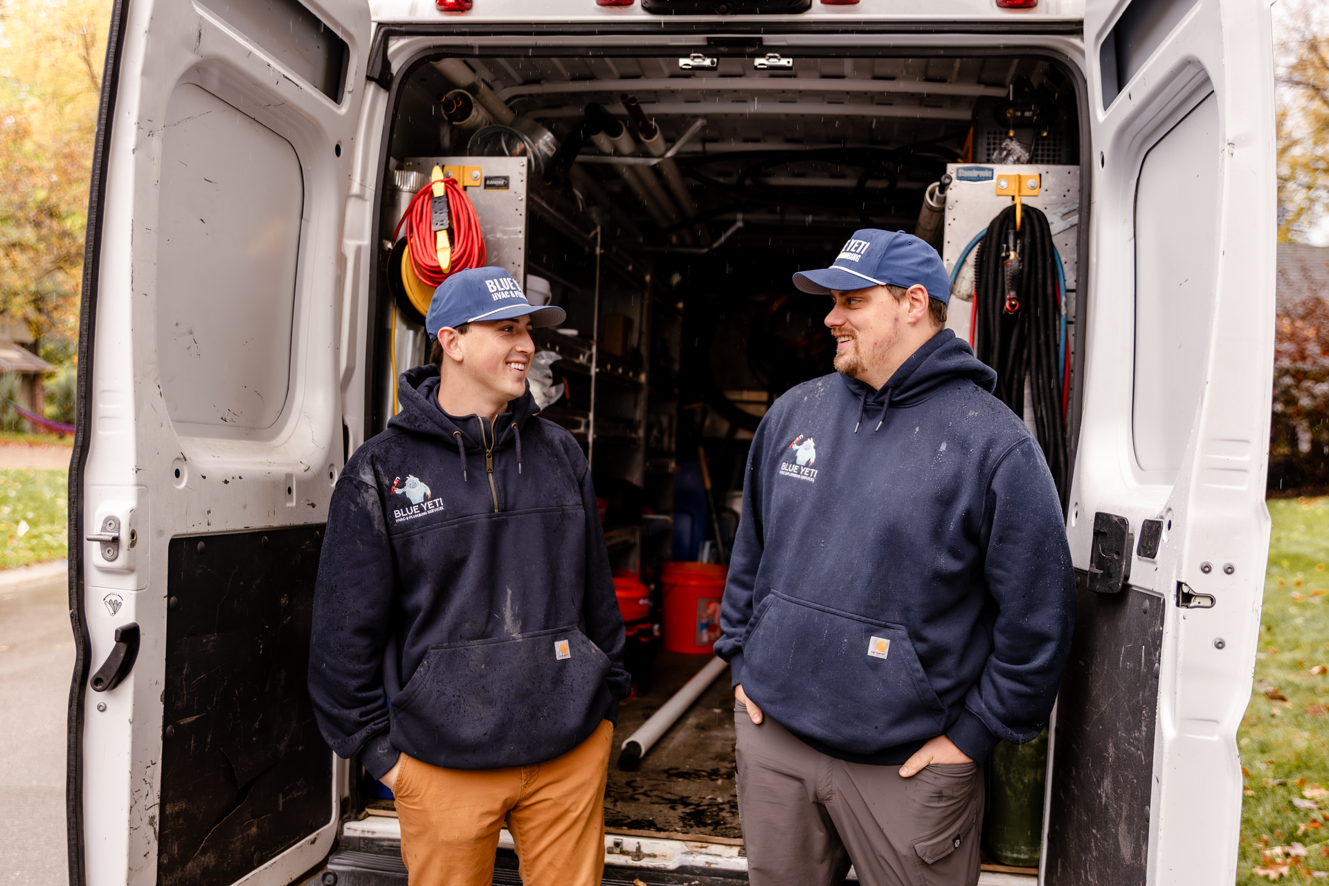 Two Blue Yeti HVAC Plumbing HVAC technicians standing in the open back of a white service van, tools visible