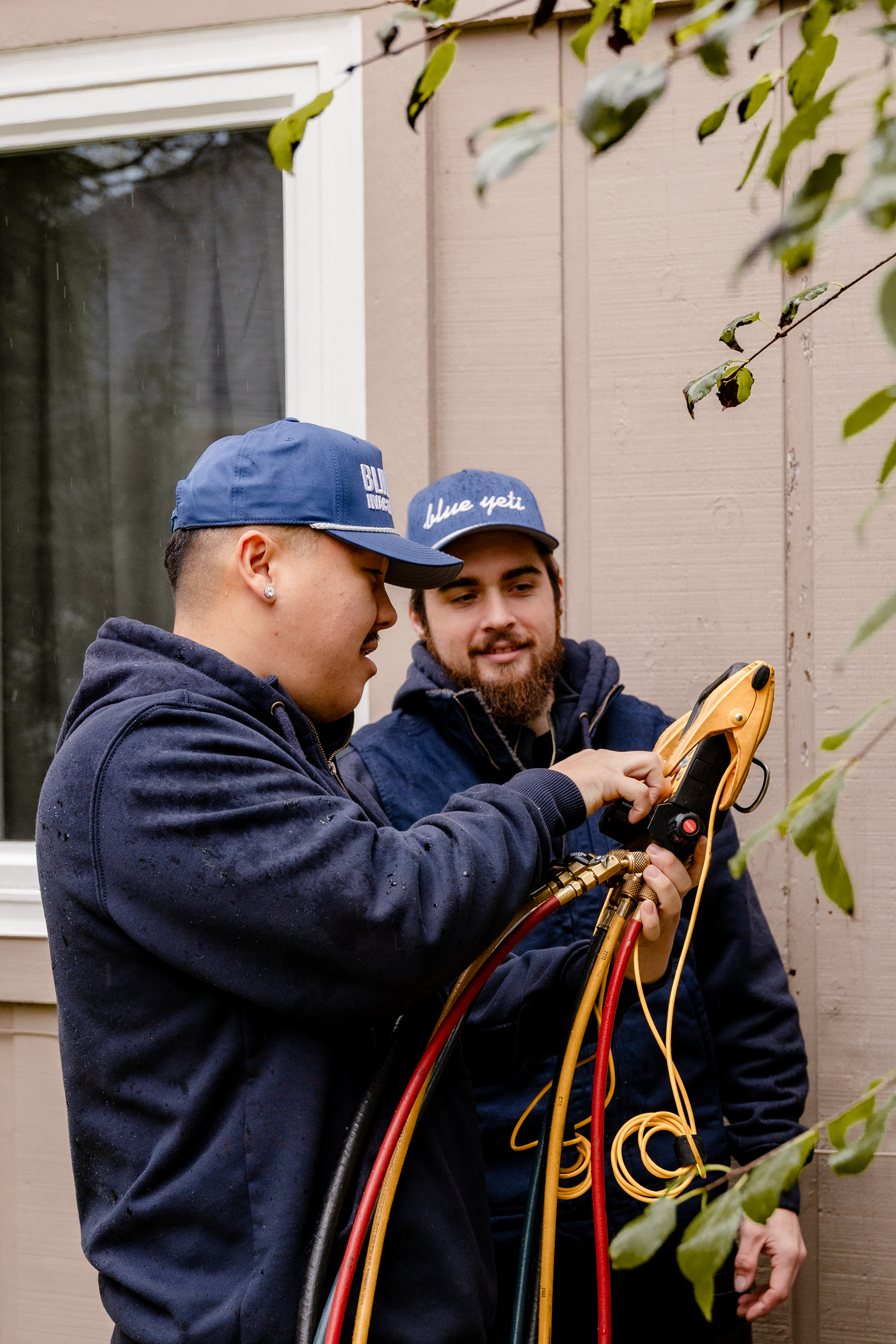 Two men in blue caps and jackets inspecting colored wires outdoors.