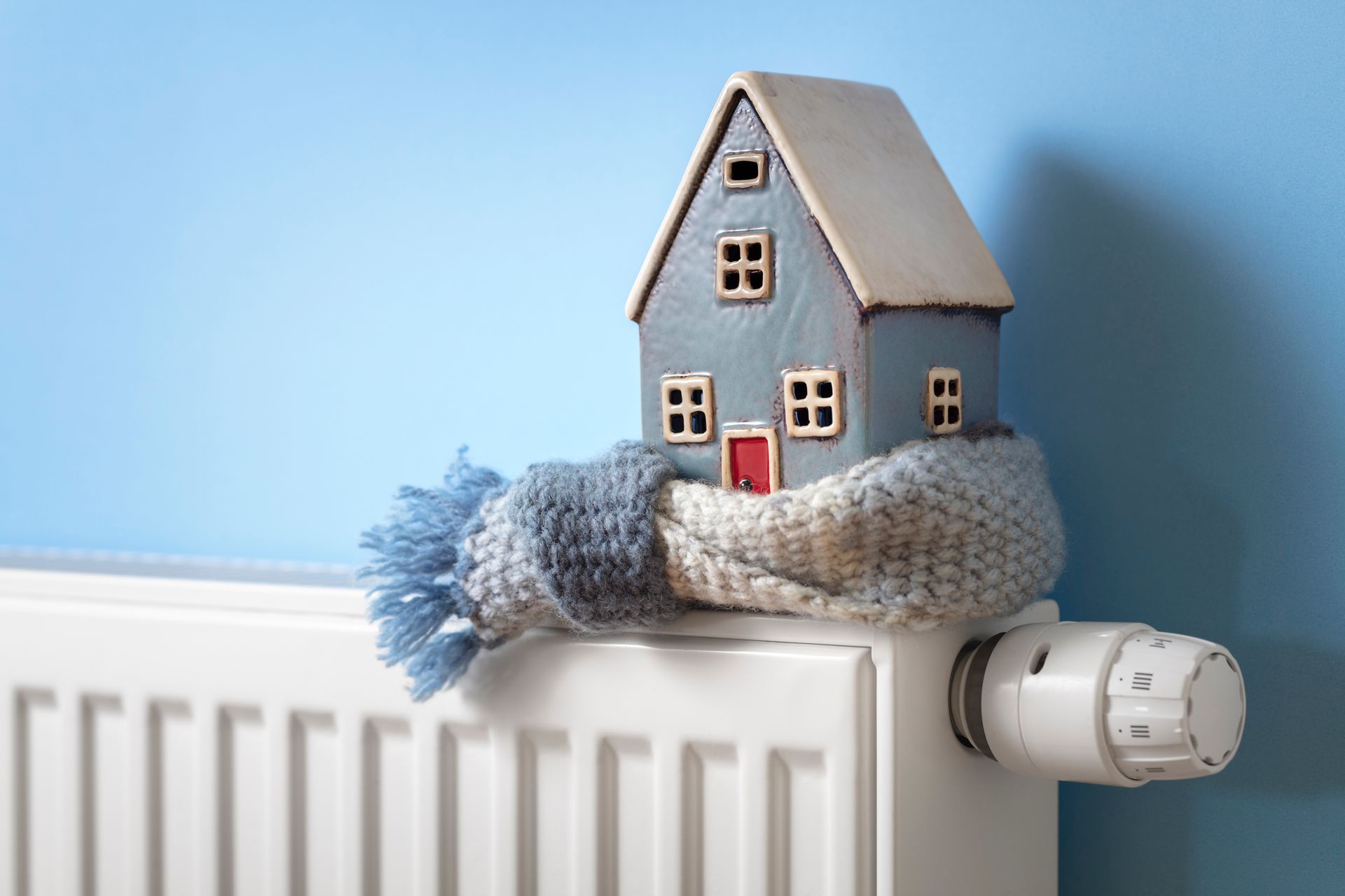 House model wrapped in scarf on radiator winter energy, heating and insulation background.