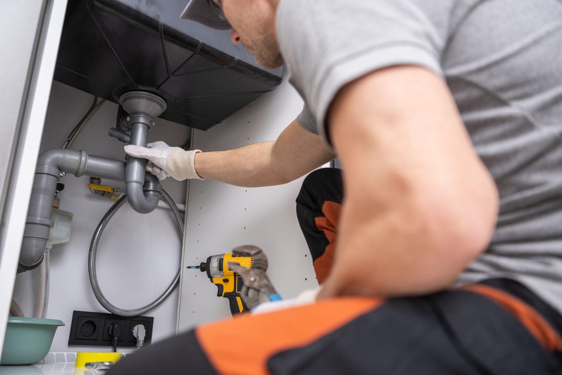 A plumber inspecting pipes under a sink for leaks, highlighting signs of water damage and mold growt