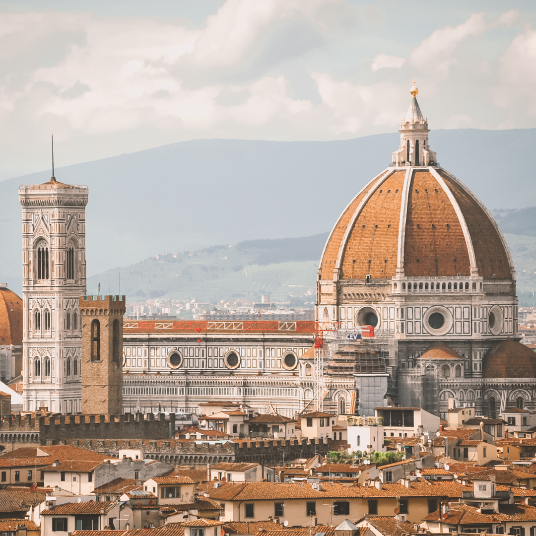 Een luchtfoto van een stad met een koepel op de voorgrond en bergen op de achtergrond.