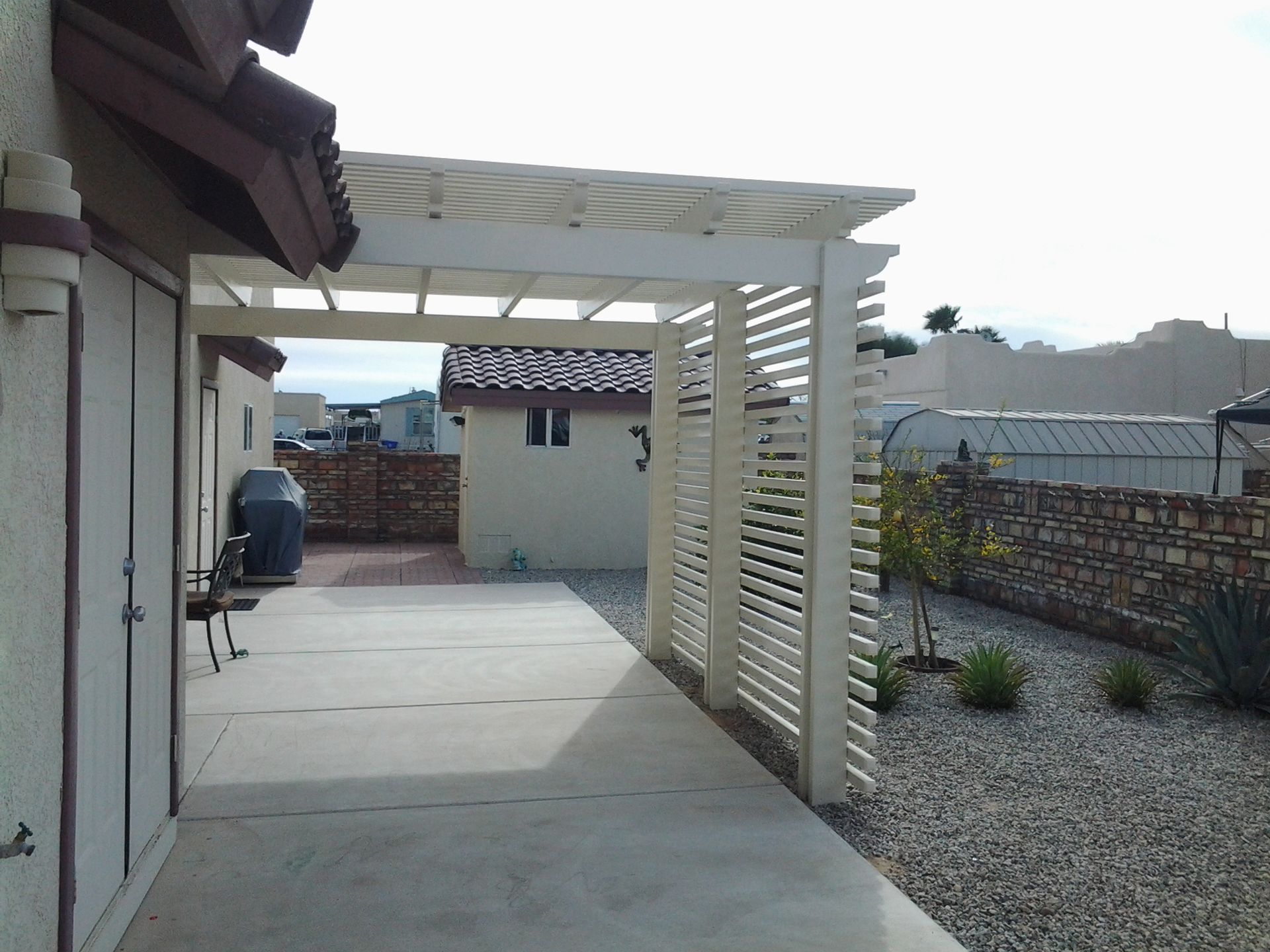 Backyard patio with a white pergola, concrete walkway, and gravel landscaping.