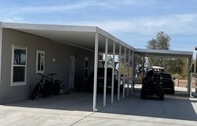 Light gray house with a covered carport; a vehicle and golf cart are parked beneath.
