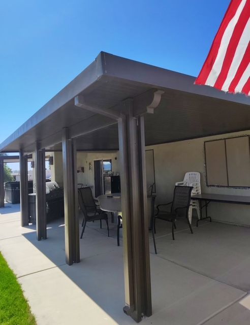 Brown patio cover with columns over outdoor seating area and American flag.
