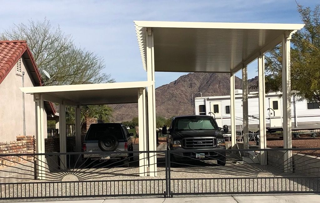Two beige carports, sheltering a pickup truck and a parked SUV, near a house and an RV.
