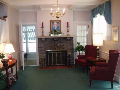 A cozy living room with a fireplace, armchairs, and a portrait over the mantel.