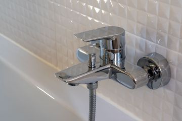 Chrome bathtub faucet with shower hose against white tiled wall