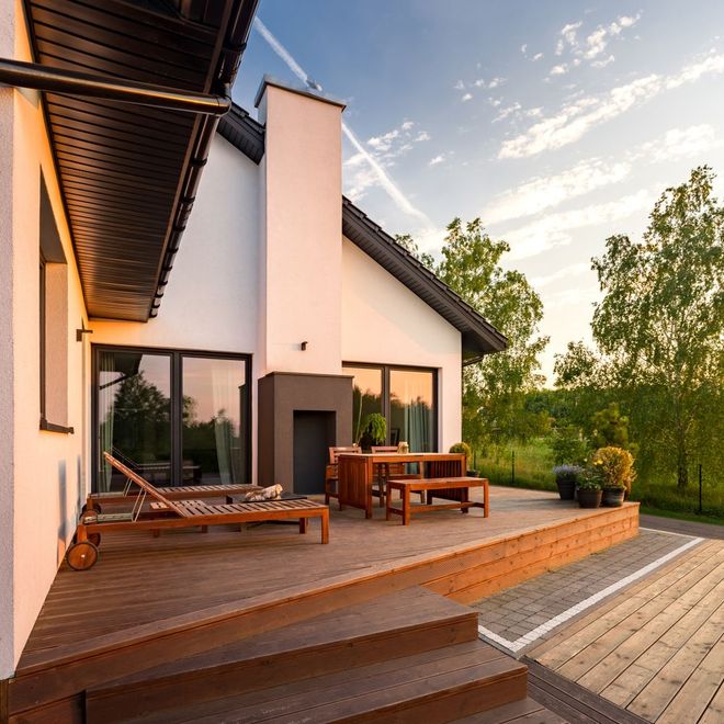 Modern house patio with wooden deck, lounge chairs, and a dining table at sunset