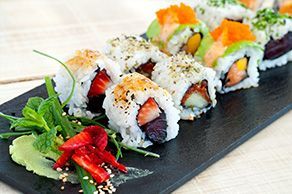Une assiette noire garnie de rouleaux de sushi et de légumes.