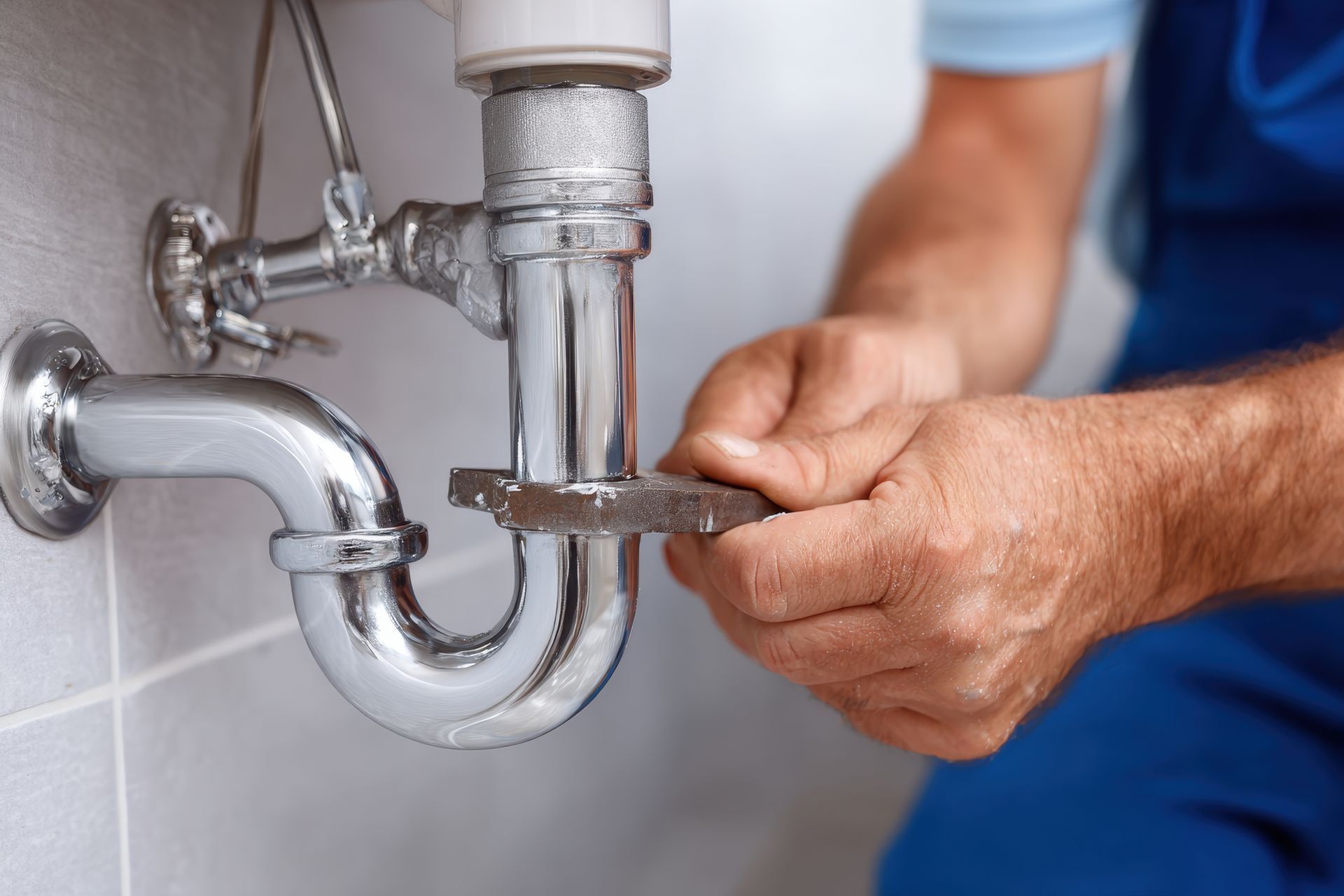 A plumber is fixing a sink pipe with a wrench.