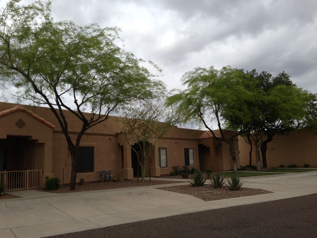 Tan stucco building with green trees in front on a cloudy day.