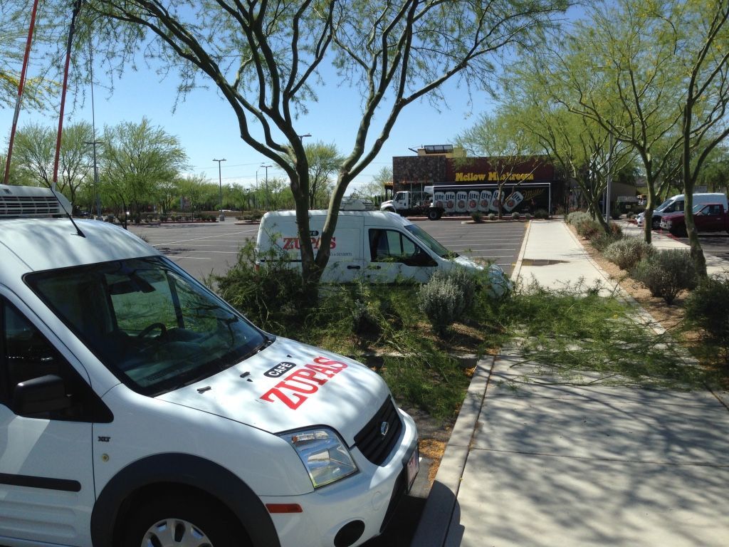 White ZURK service van parked by a curb with other vehicles in a commercial parking lot under a blue sky.