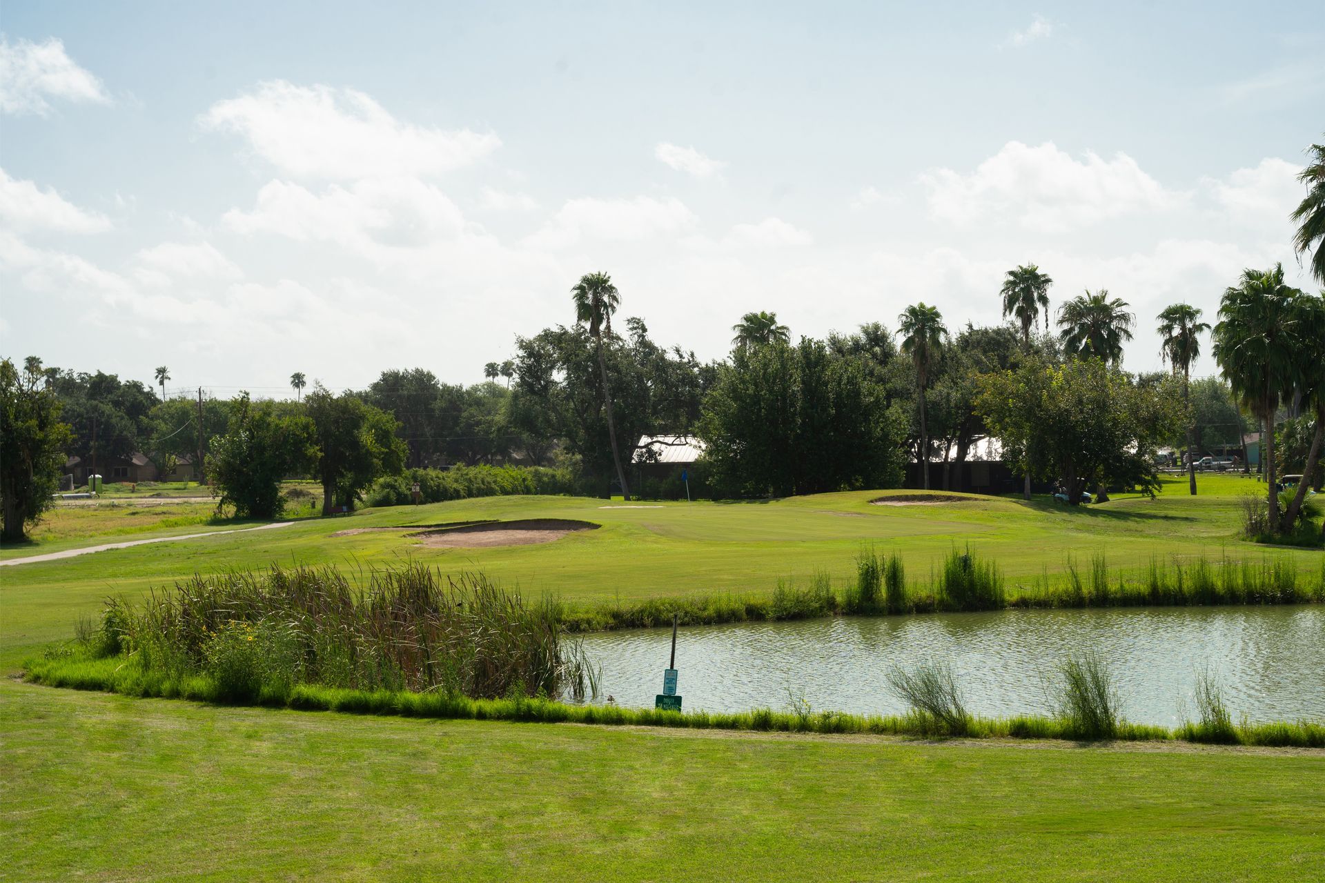 Golf course with water feature, green grass, trees, and blue sky.