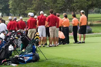 Golfers in red and orange shirts on a green golf course, standing near their golf bags.