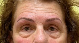 A close up of a woman 's face with a tattoo on her eyebrows.