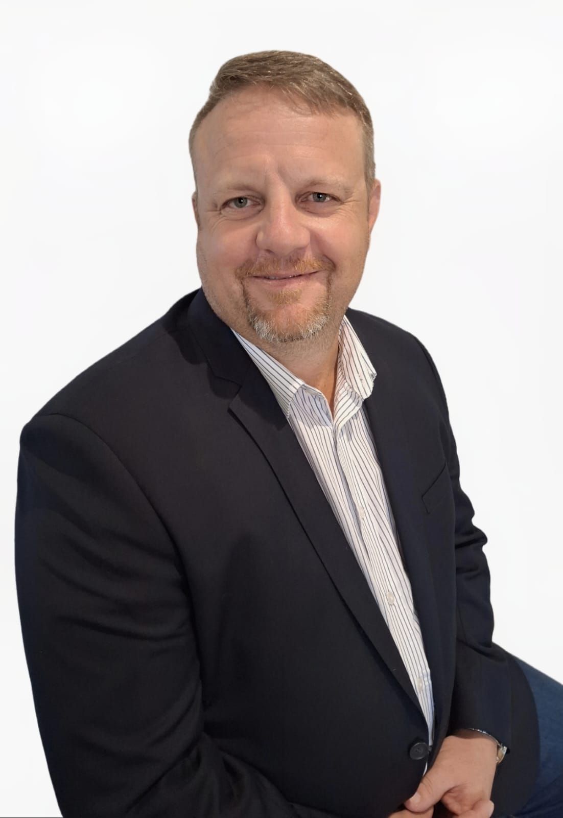 A man in a suit and white shirt is sitting in front of a white background.