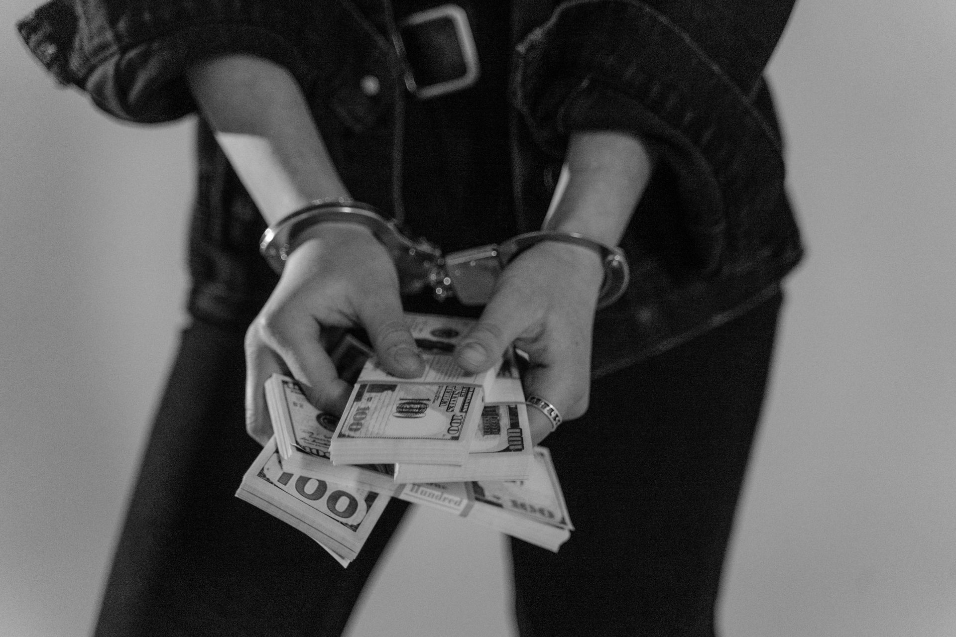 A woman in handcuffs is holding a stack of money.