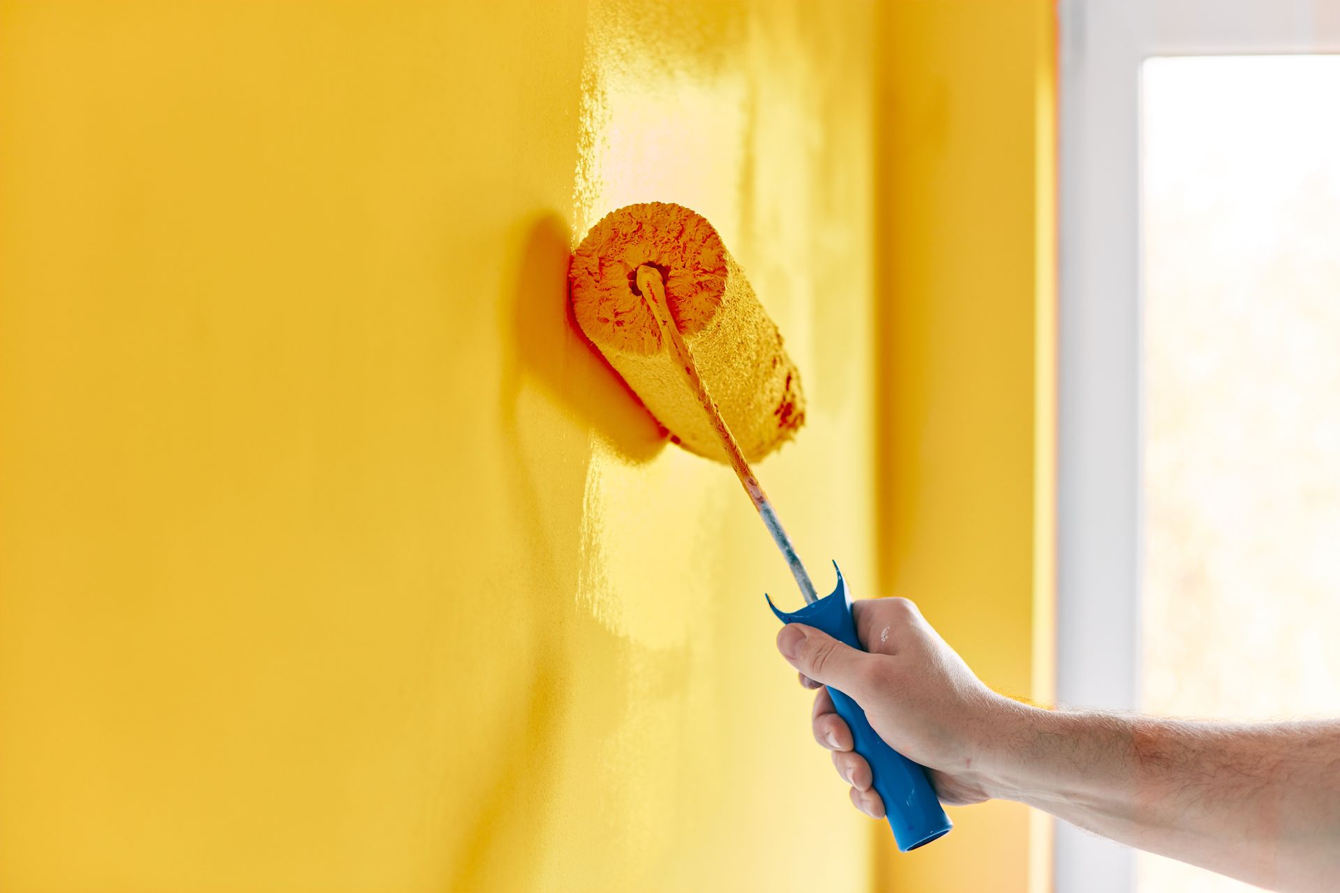 a person is painting a yellow wall with a paint roller