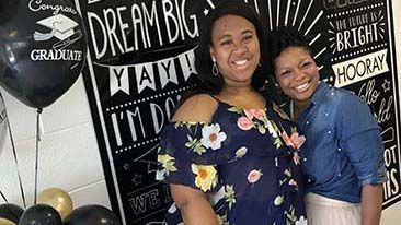 two women are posing for a picture in front of a chalkboard with balloons .