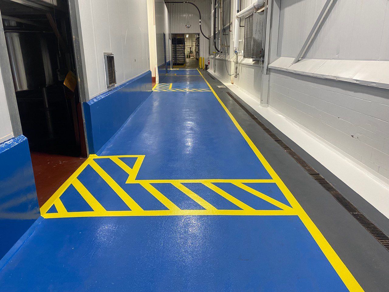 a warehouse section that required a safty pathway where machniery is not allowed to pass. this pathe way was created using blue epoxy with yellow lines indicating where material cant be left. the wall sides also have a clear coat of epoxy finish.