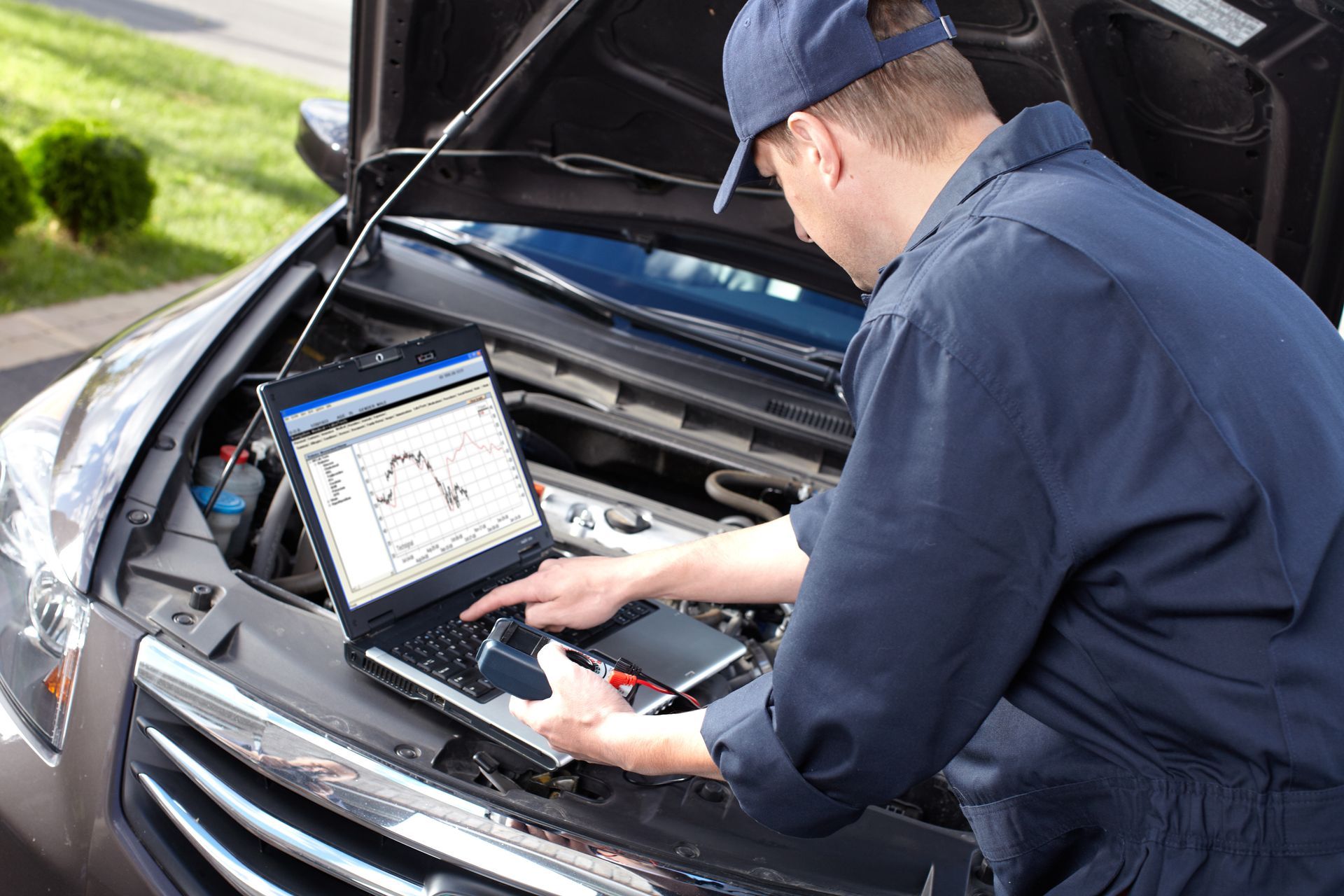 Mechanic using a laptop under the hood of a car during diagnostics