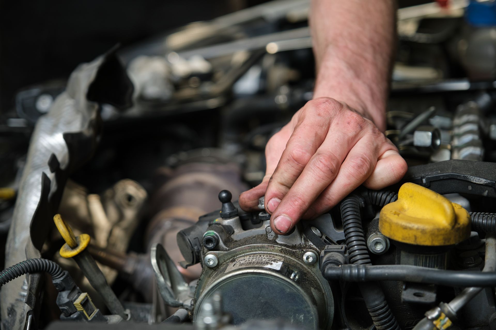 Hand adjusting a car engine component in an open hood, with yellow oil cap visible