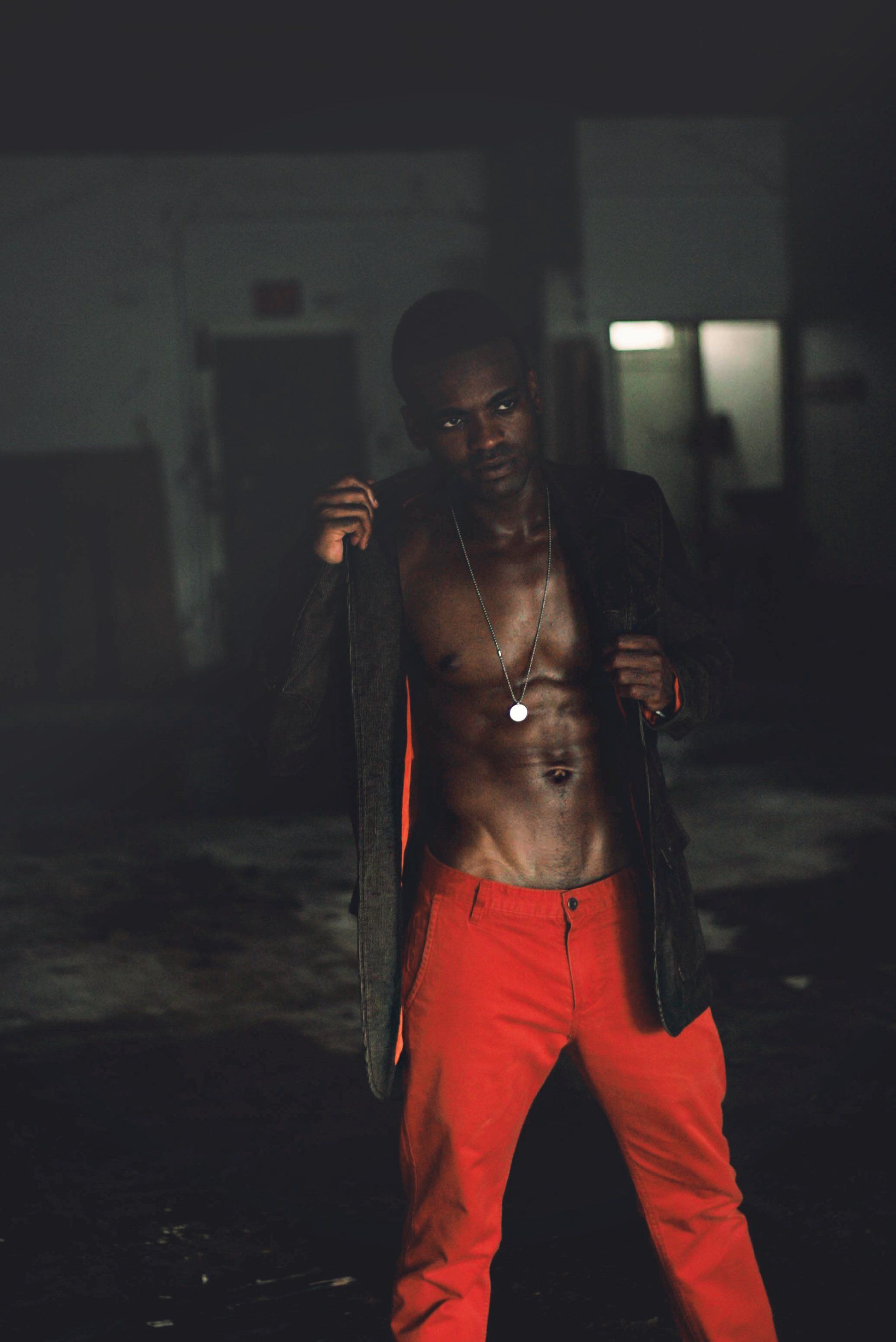 MLN in red pants and a black jacket is standing in the dark.
