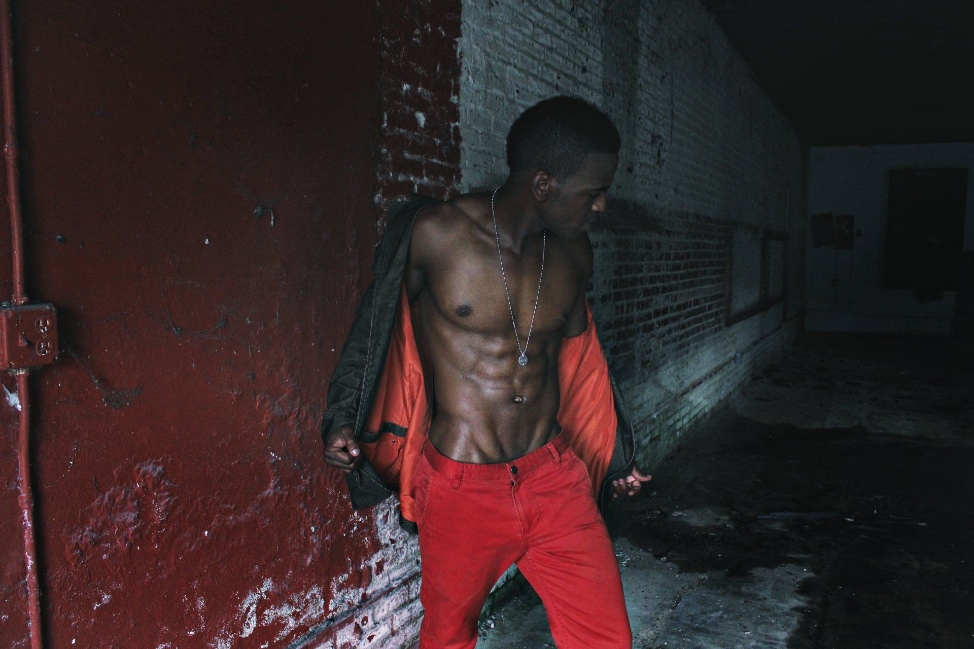 MLN in red pants is standing in front of a brick wall.