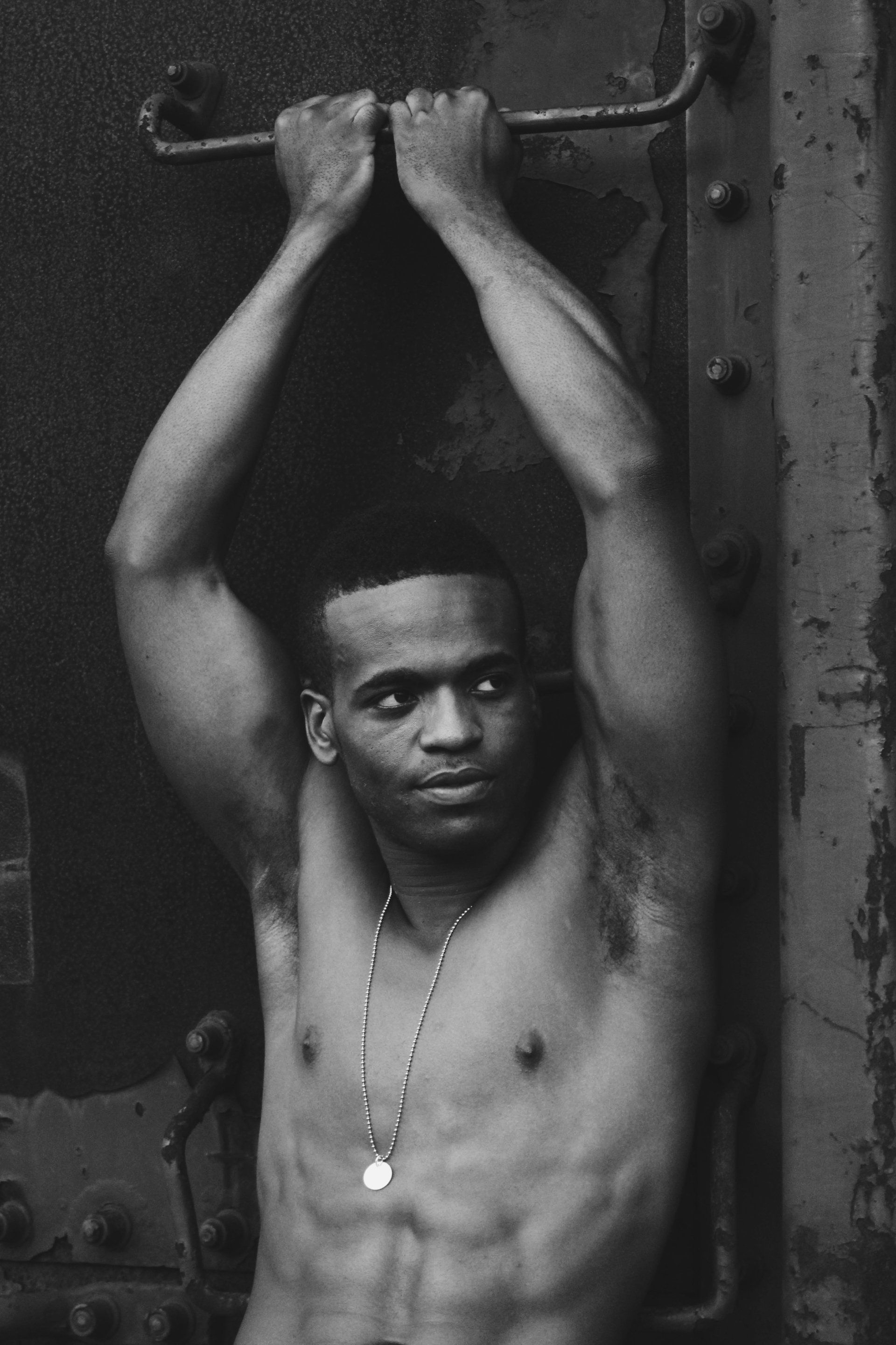 A black and white photo of a shirtless man hanging on a train box car