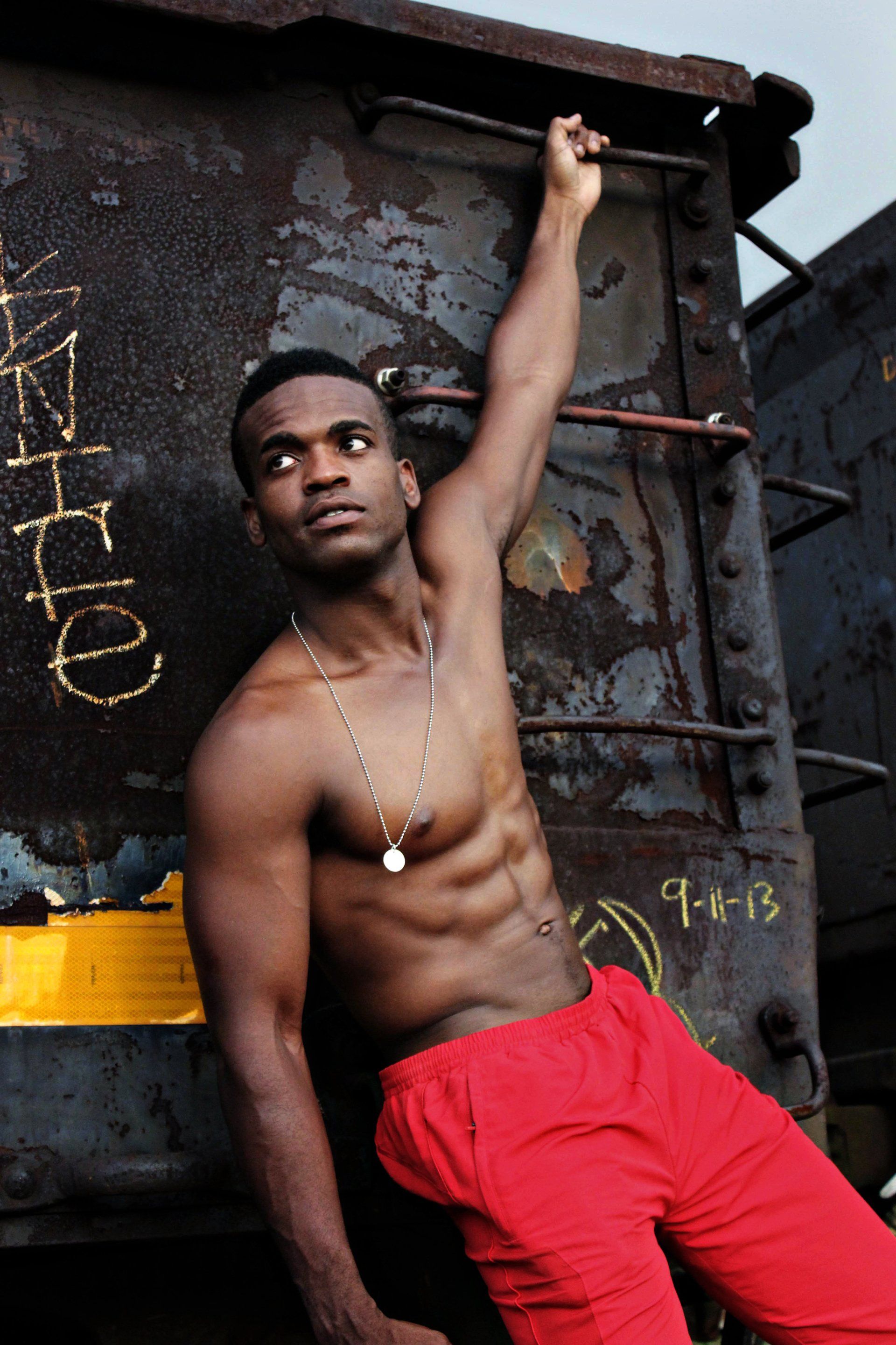 A shirtless man in red shorts leans against a rusty wall with the number 9 on it