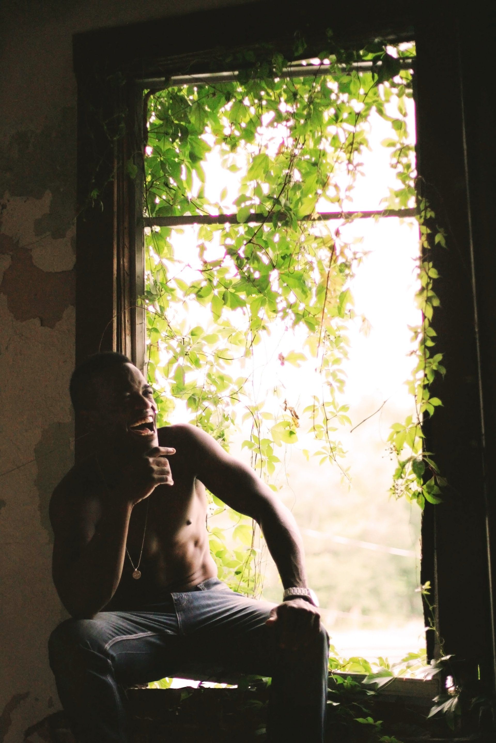 A laughing man sits on a window sill looking out