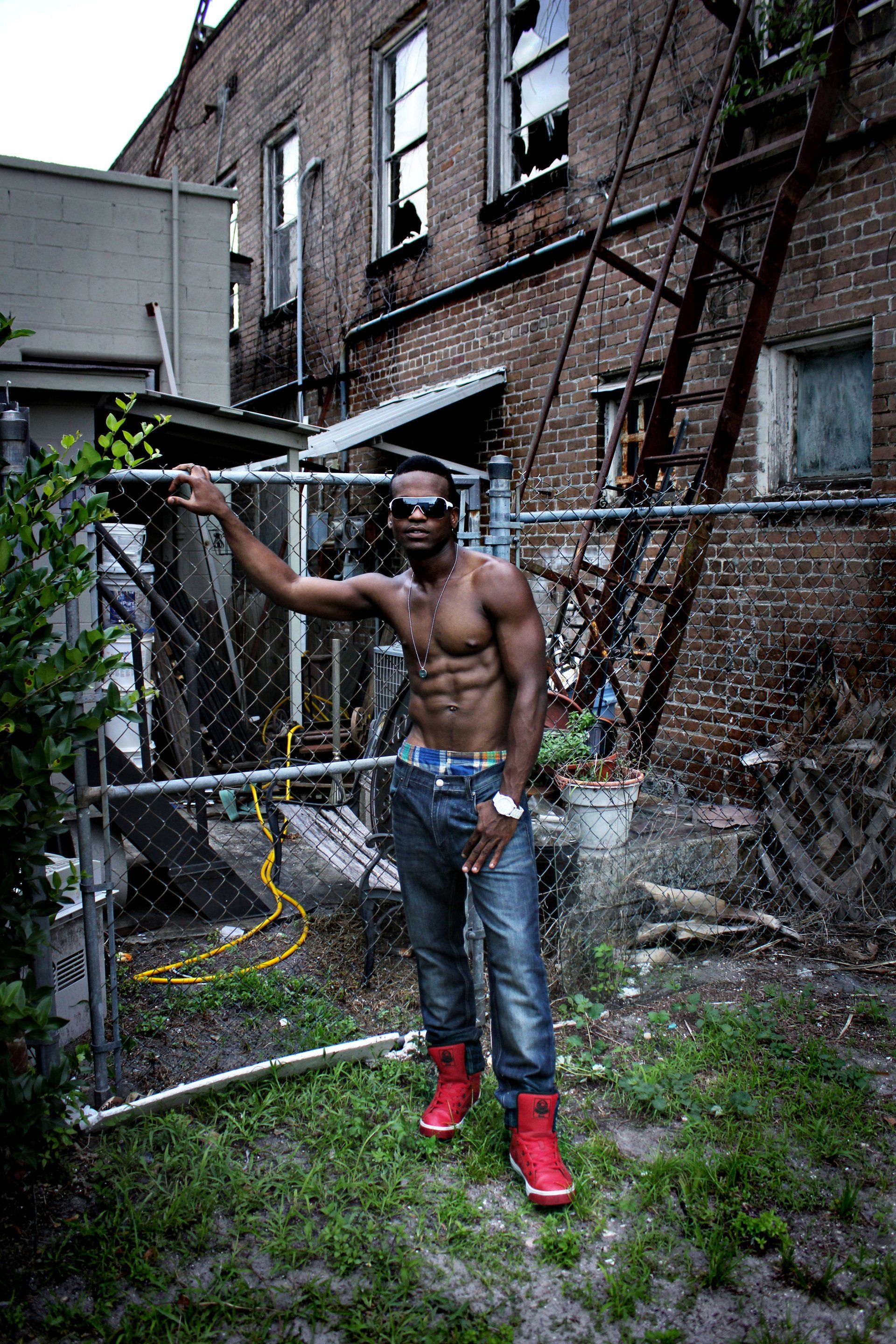 MLN leaning on a chain link fence in front of a brick building.